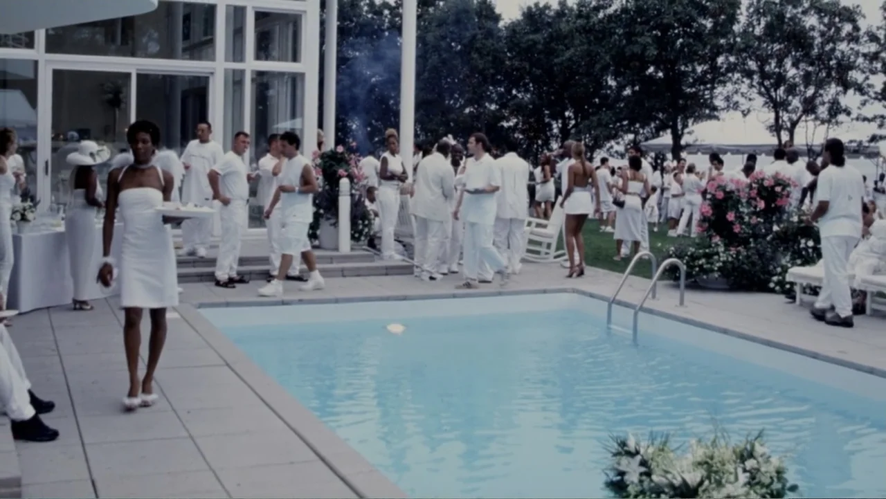 Diddy: The Making of a Bad Boy (2025) movie still: wide — A crowded outdoor patio area with a swimming pool surrounded by people in white clothing.…