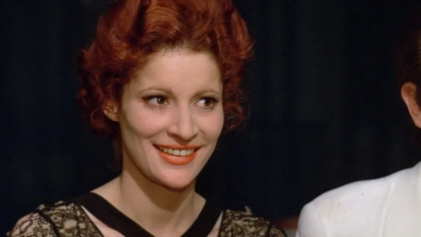Tenderness of the Wolves (1973) movie still: closeup — A dimly lit indoor setting with a dark backdrop behind the subjects. A woman with red hair…