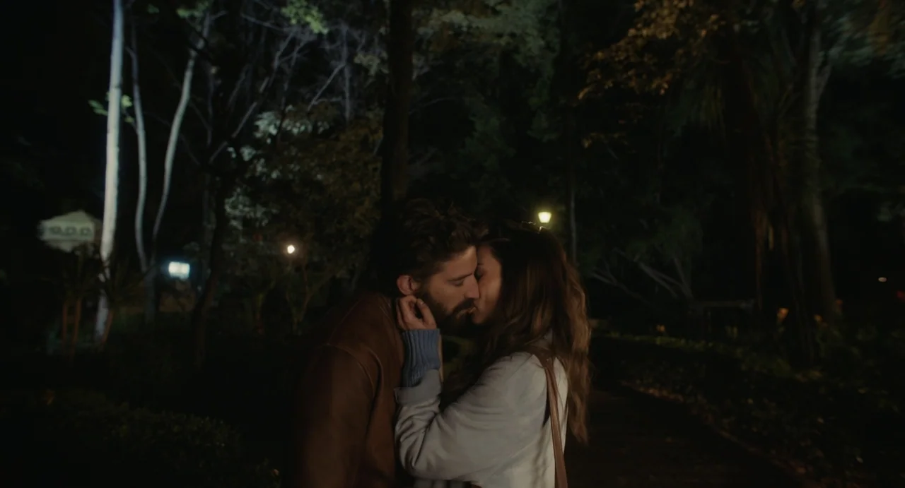 Dating Santa (2023) movie still: medium — A dark park at night with dense trees visible in the background. A man and a woman stand close to each…
