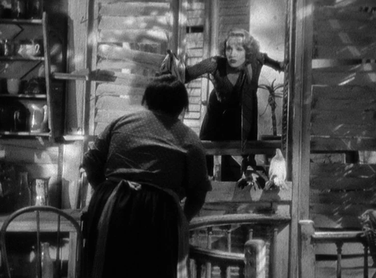 Blonde Venus (1932) movie still: medium — A rustic wooden room features slatted window shutters casting striped light across the interior. A woman…