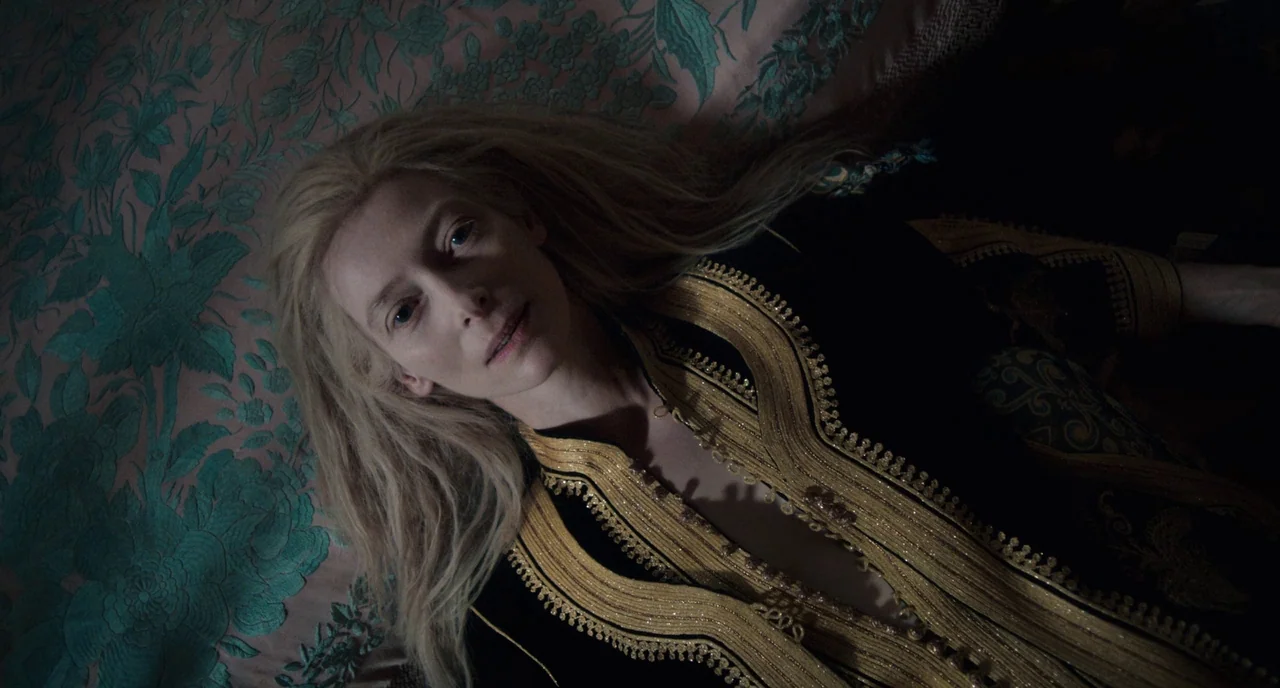Only Lovers Left Alive (2013) movie still: closeup — A woman lies on a bed with a pink floral-patterned fabric surface. She rests on her back…
