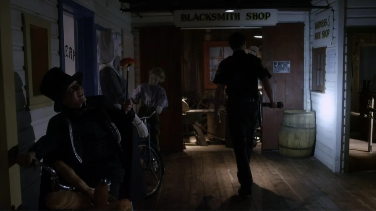 Jinxed (2013) movie still: medium — A dimly lit museum hallway displays mannequins in historic clothing inside alcoves. A security guard in a dark…
