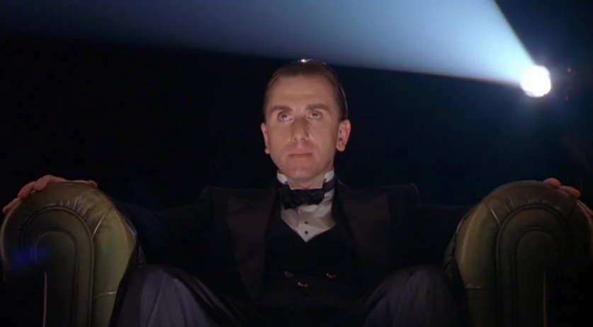 Invincible (2001) movie still: medium — A dark, empty cinema hall features a man seated in a leather armchair. The man looks forward toward a light…