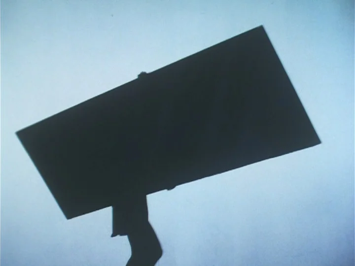 Butterfly (1974) movie still: wide — A dark silhouette of a person appears against a uniform light blue background. The subject carries a large…