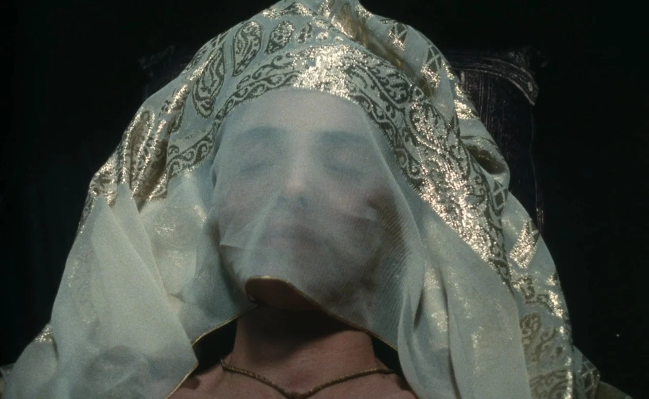 The Pit and The Pendulum (1991) movie still: closeup — A woman lies against a dark surface while draped in an ornate fabric veil. The sheer…