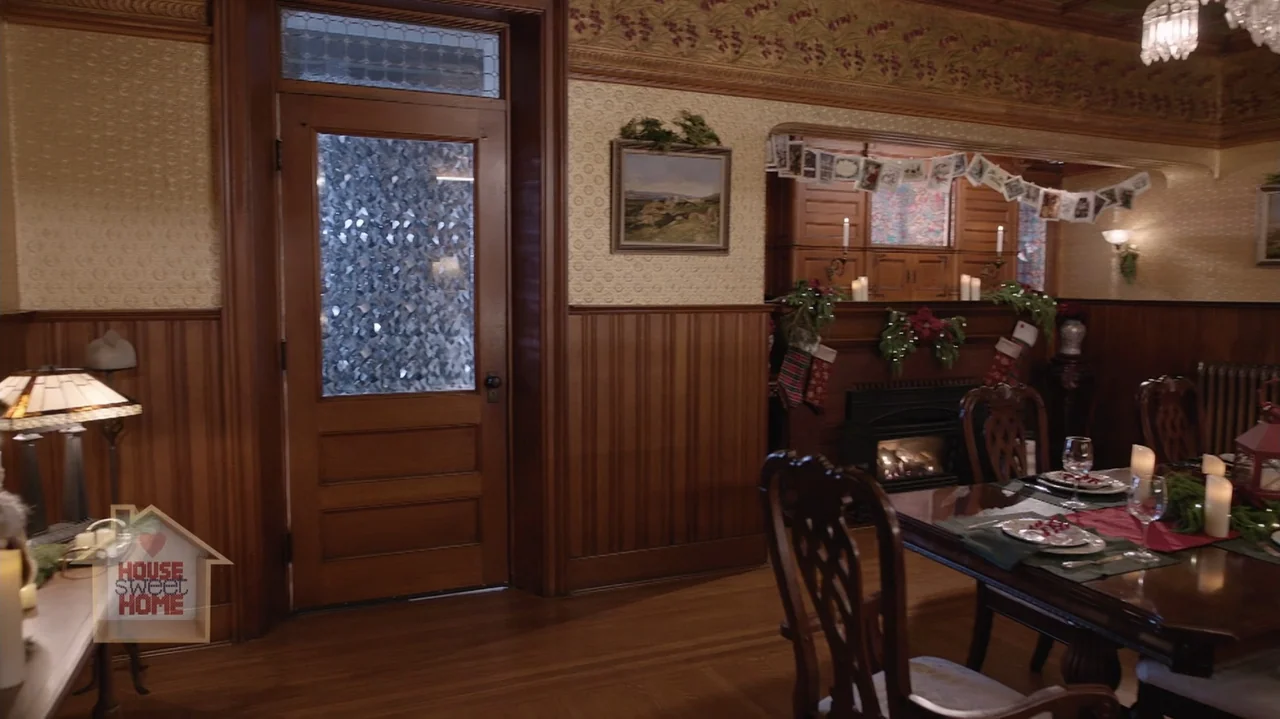 Designing Christmas (2022) movie still: wide — An interior dining area featuring wood paneled walls and decorative holiday garland displays. The…