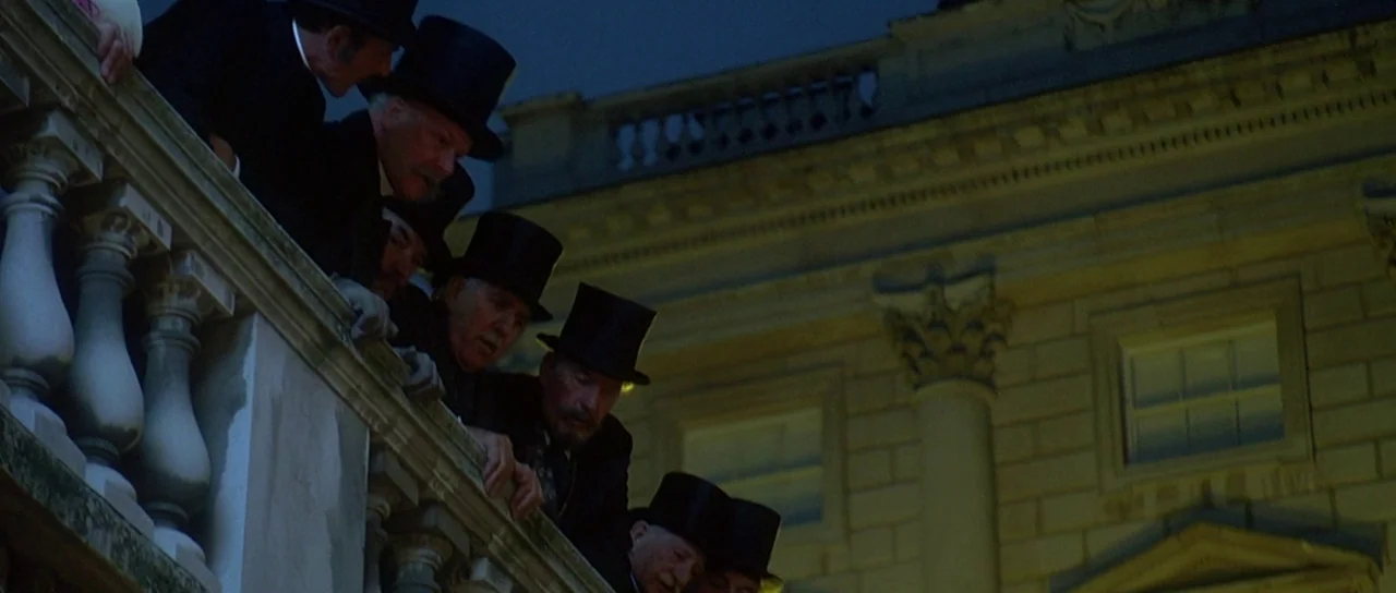 The Portait of a Lady (1996) movie still: medium — A group of men in top hats lean over a stone balcony at night. The classical architectural facade…