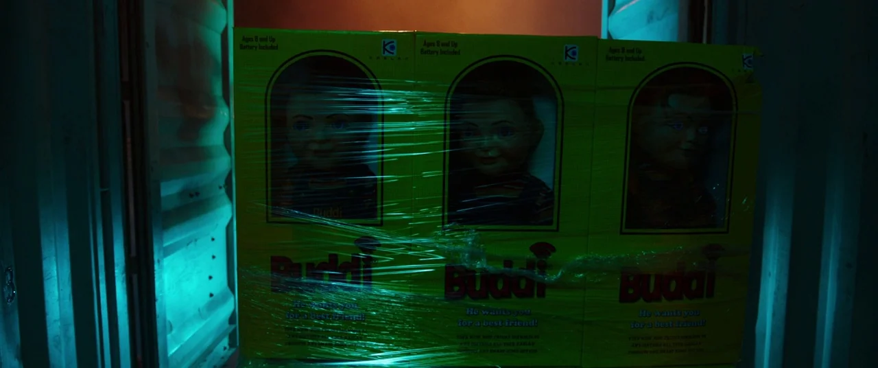 Child's Play (2019) movie still: medium — Three product boxes are shrink-wrapped together inside a dark, ribbed metal shipping container. The…