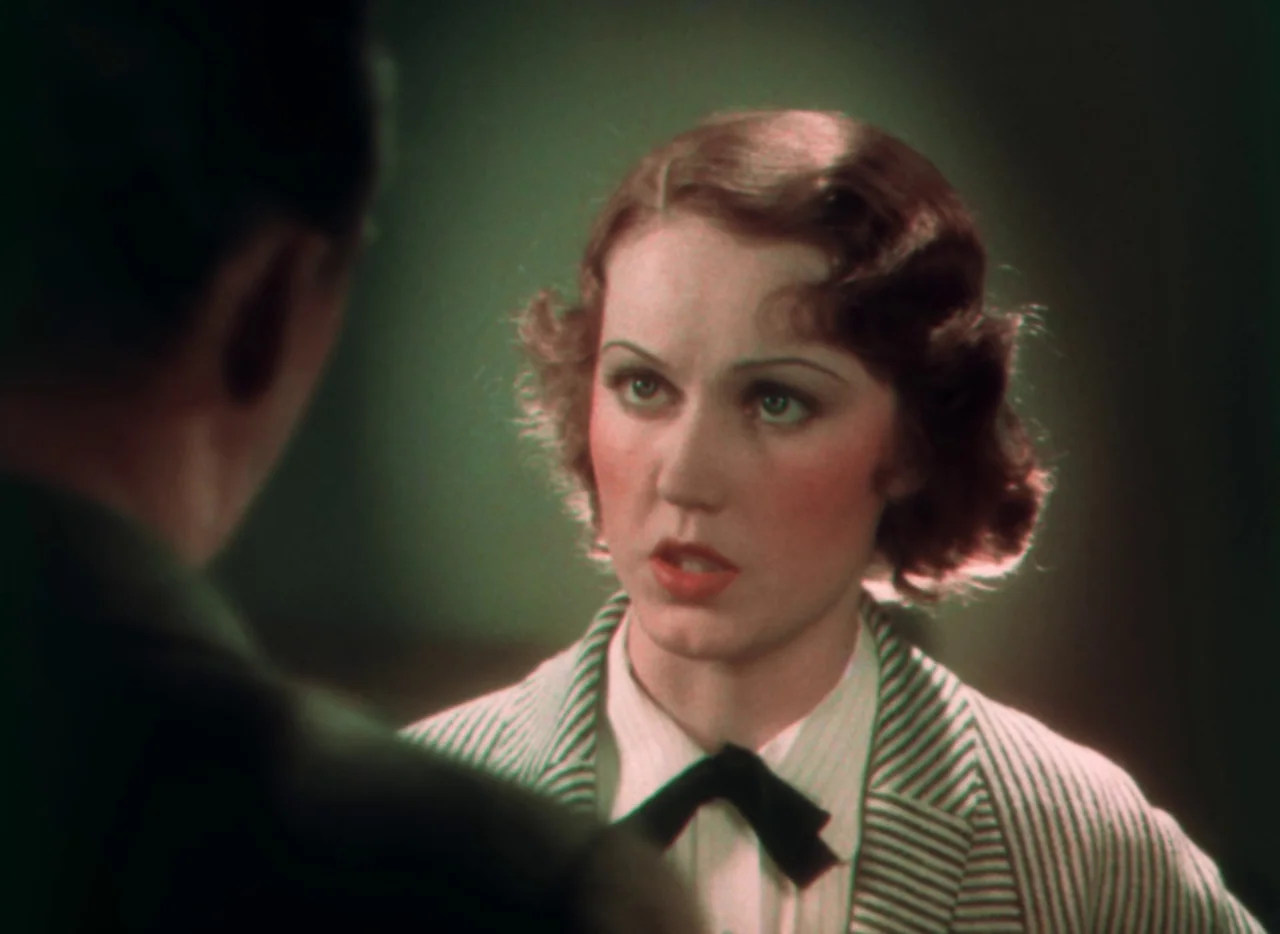 Doctor X (1932) movie still: closeup — A woman with wavy hair stands in a dimly lit indoor space. She faces an unseen person while wearing a striped…