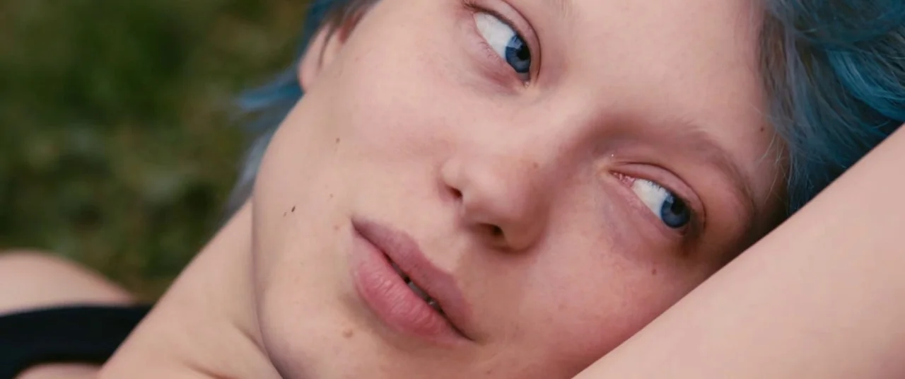 Blue Is The Warmest Colour (2013) movie still: closeup — A woman lies on a grassy surface outdoors during the day. She looks towards the right while…
