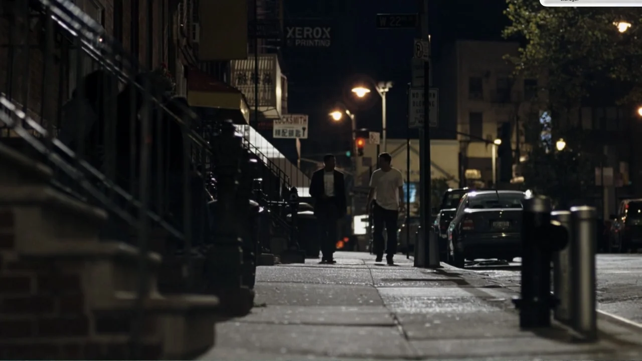 Fighting (2009) movie still: wide — A nighttime city street features brick row houses, metal railings, and parked cars. Two men walk towards the…