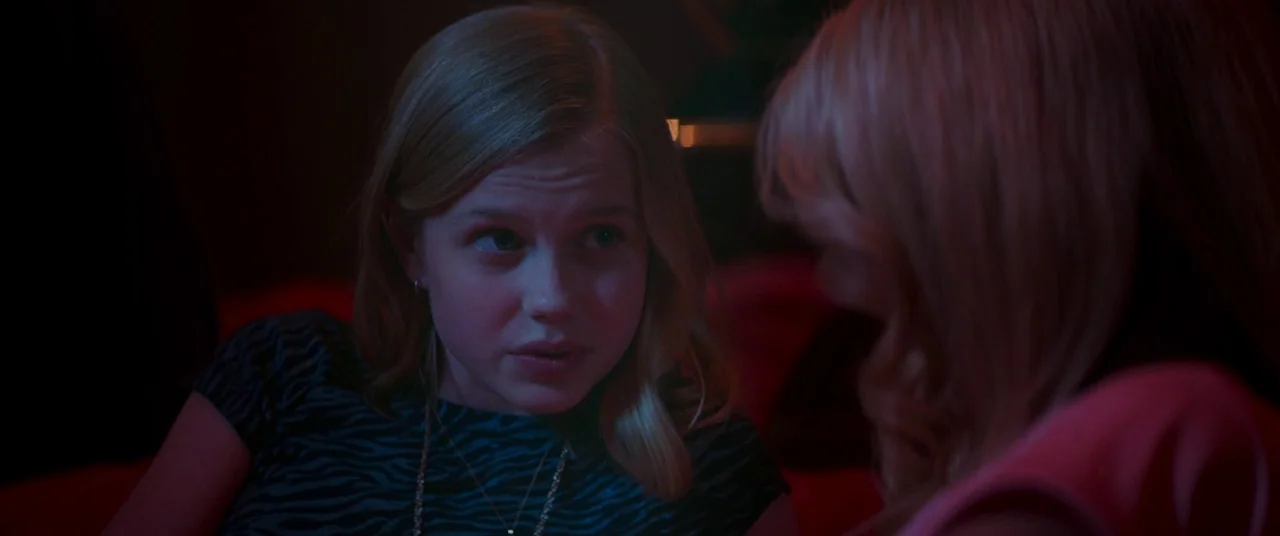 The Nice Guys (2016) movie still: medium — A dimly lit room with two young women conversing in near darkness. Red and blue ambient light illuminates…