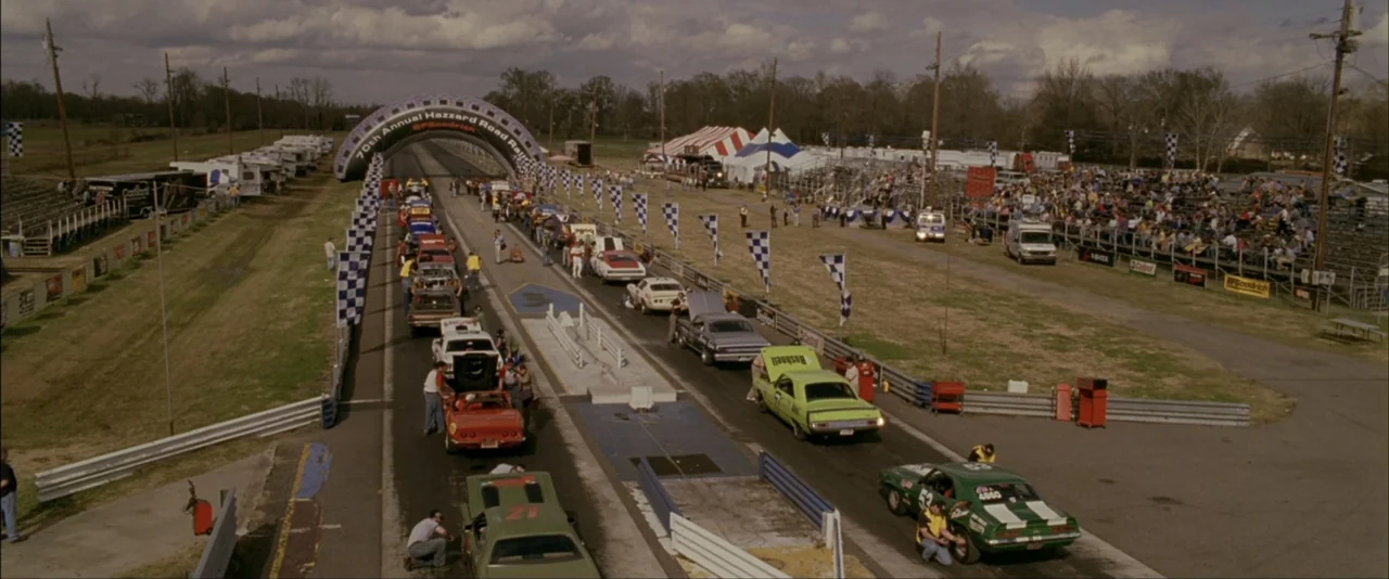 The Dukes of Hazzard (2005) movie still: establishing — An outdoor drag racing event features numerous classic muscle cars staged on a track.…