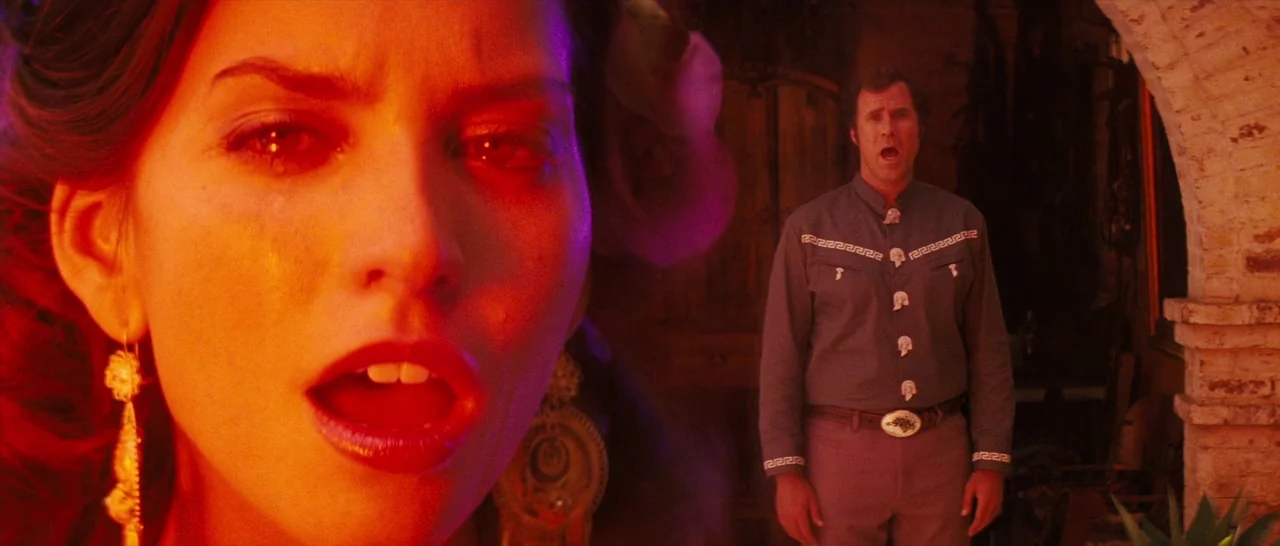 Casa De Mi Padre (2012) movie still: medium — A stone courtyard with arched brick doorways is bathed in intense, saturated red light. A woman is in…