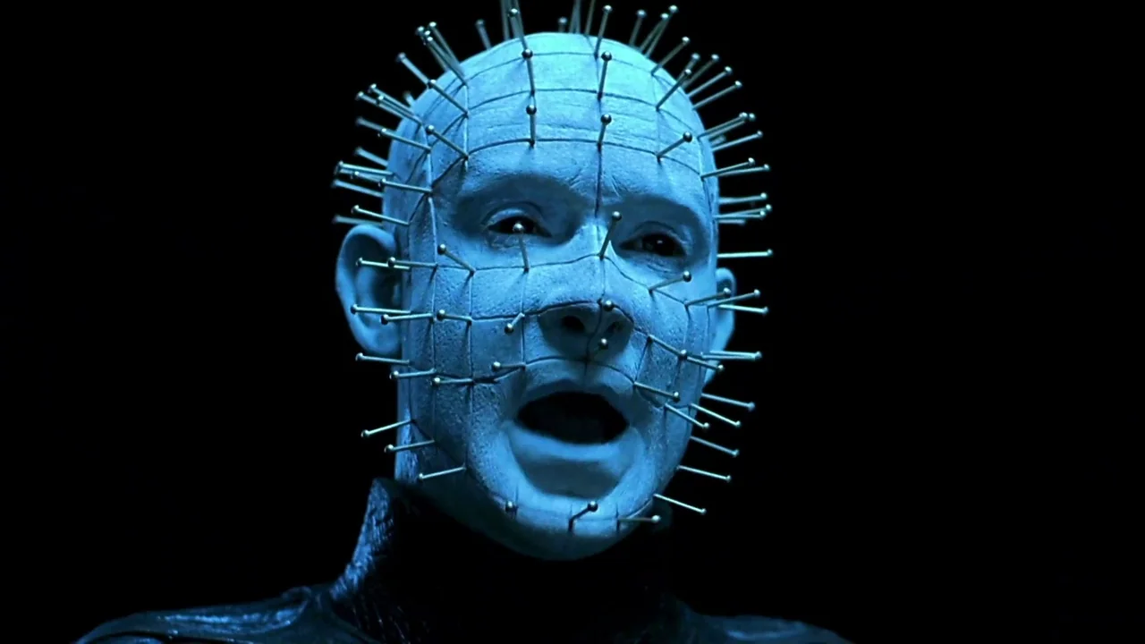 Hellraiser: Inferno (2000) movie still: closeup — A figure with a pale head pierced by metal needles emerges from black darkness. The character…