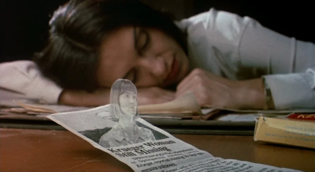 Freddy’s Dead: The Final Nightmare (1991) movie still: closeup — A woman rests her head on a wooden desk covered in papers. A newspaper clipping…