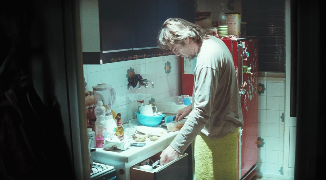 Biutiful (2010) movie still: medium — A cluttered domestic setting features white-tiled walls decorated with flower-shaped stickers. A man stands at…