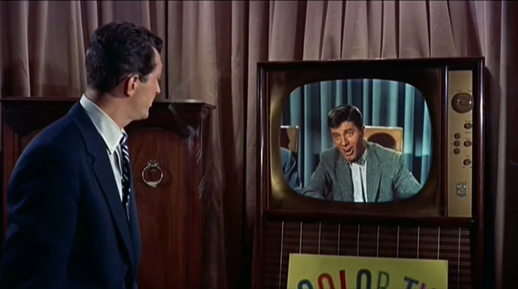 Artists and Models (1955) movie still: medium — A man stands in a room with draped fabric walls watching a vintage television. The television…