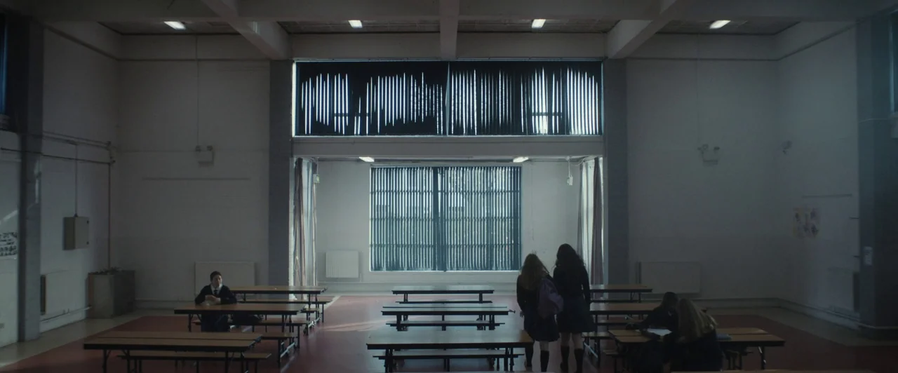 You Are Not My Mother (2021) movie still: wide — A spacious school dining hall features rows of wooden tables on a red floor. Students are scattered…