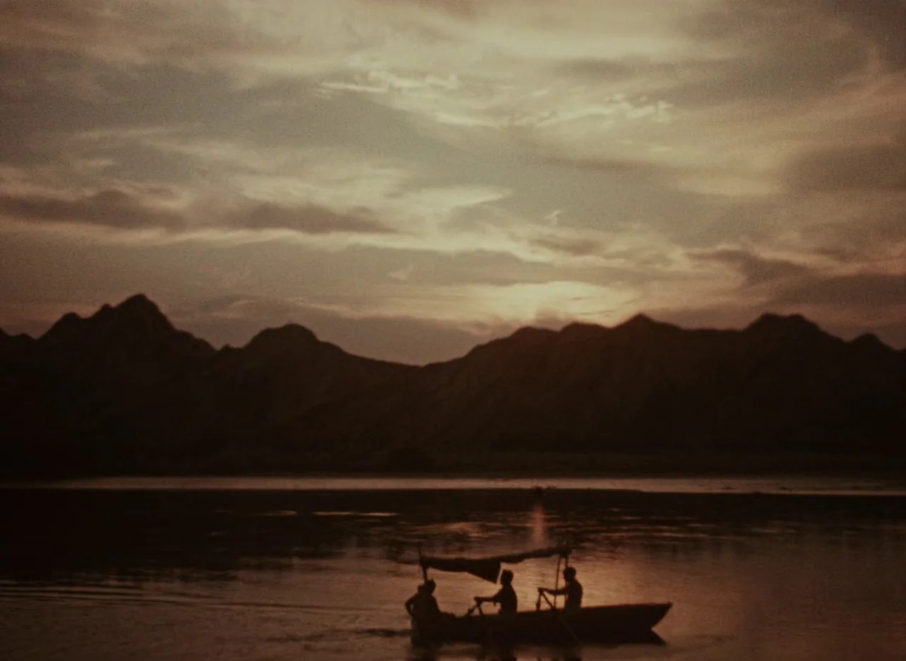 A Journey to the Beginning of Time (1955) movie still: wide — A wide river flows in front of dark, silhouetted mountains during a sunset. Three…