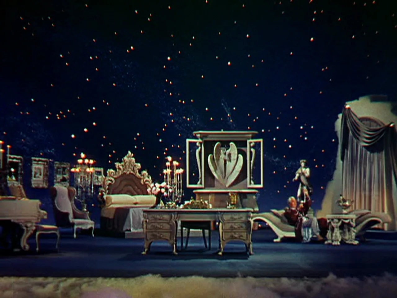Ziegfeld Follies (1945) movie still: wide — A surreal room features elaborate furniture pieces set against a dark night sky background. A man rests…