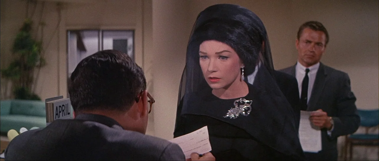 What A Way To Go! (1964) movie still: medium — An office reception area features light walls and a calendar block labeled April. A woman in a black…