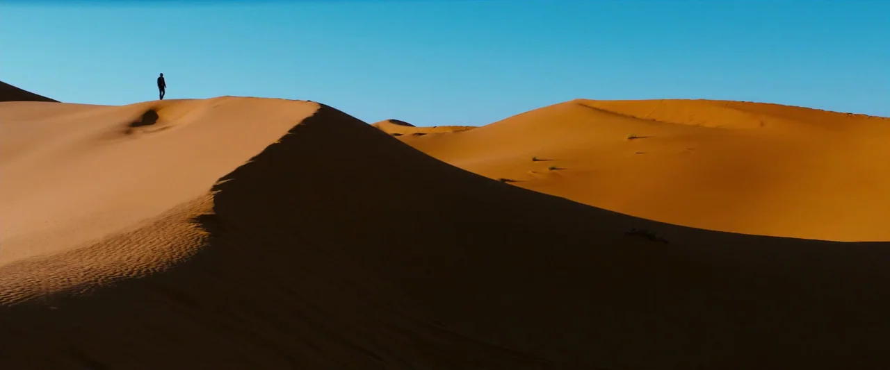 John Wick: Chapter 3 – Parabellum (2019) movie still: wide — Extensive rolling sand dunes stretch across a vast landscape under a clear sky. A lone…