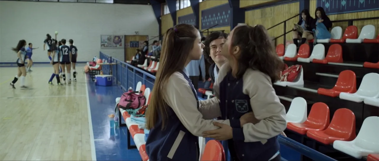 Disconnected 2 (2025) movie still: medium — An indoor gymnasium with bleacher seating and a wooden sports court background. Three teenagers interact…