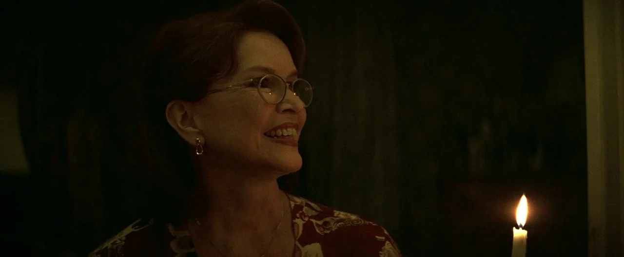 The Yards (2000) movie still: closeup — A dimly lit interior room at night provides a dark, shadowed background. A woman in a patterned blouse…