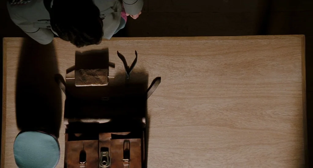 Valkyrie (2008) movie still: wide — A clean wooden surface holds a leather briefcase, a blue cap, and metal tools. A person in a military uniform…