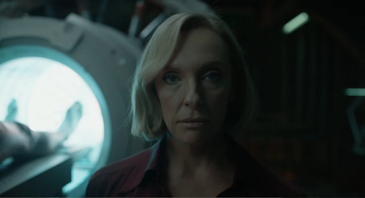 Mickey 17 (2025) movie still: closeup — A dark, industrial-style medical facility features large circular equipment glowing with internal blue…
