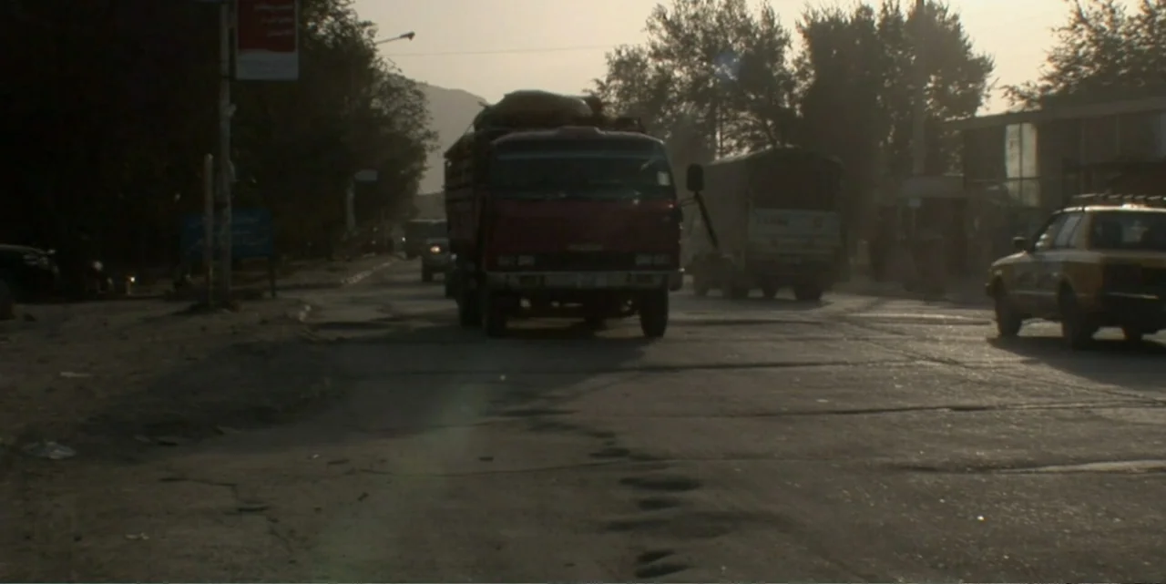 Silencing the Song: An Afghan Fallen Star (2011) movie still: wide — A dusty paved road stretches toward the horizon with sparse trees on both…