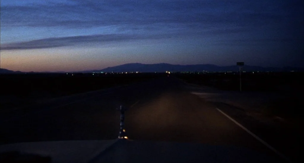 Melvin & Howard (1980) movie still: establishing — A long, dark desert road extends toward a distant horizon under a twilight sky. Mountain…