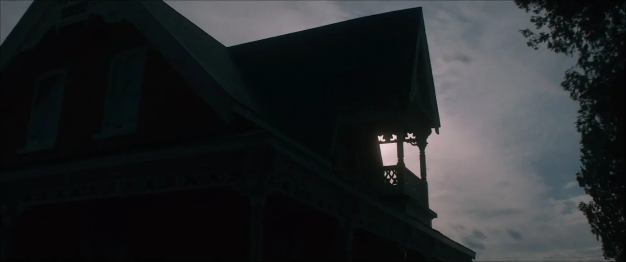I'll Take Your Dead (2018) movie still: establishing — A dark Victorian house with a gabled roof and decorative trim stands against twilight. The…