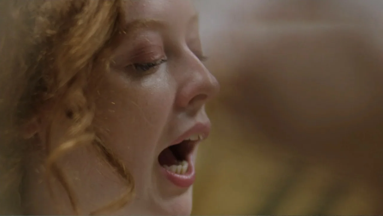 The African Desperate (2022) movie still: closeup — A close-up view focuses on a woman's face within an indeterminate indoor space. She keeps her…