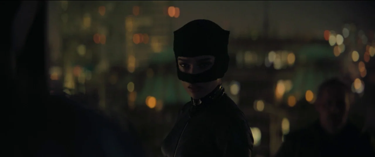 The Batman (2022) movie still: medium — A dark rooftop overlooks a distant city skyline glowing with out-of-focus light spots. A woman in a black…