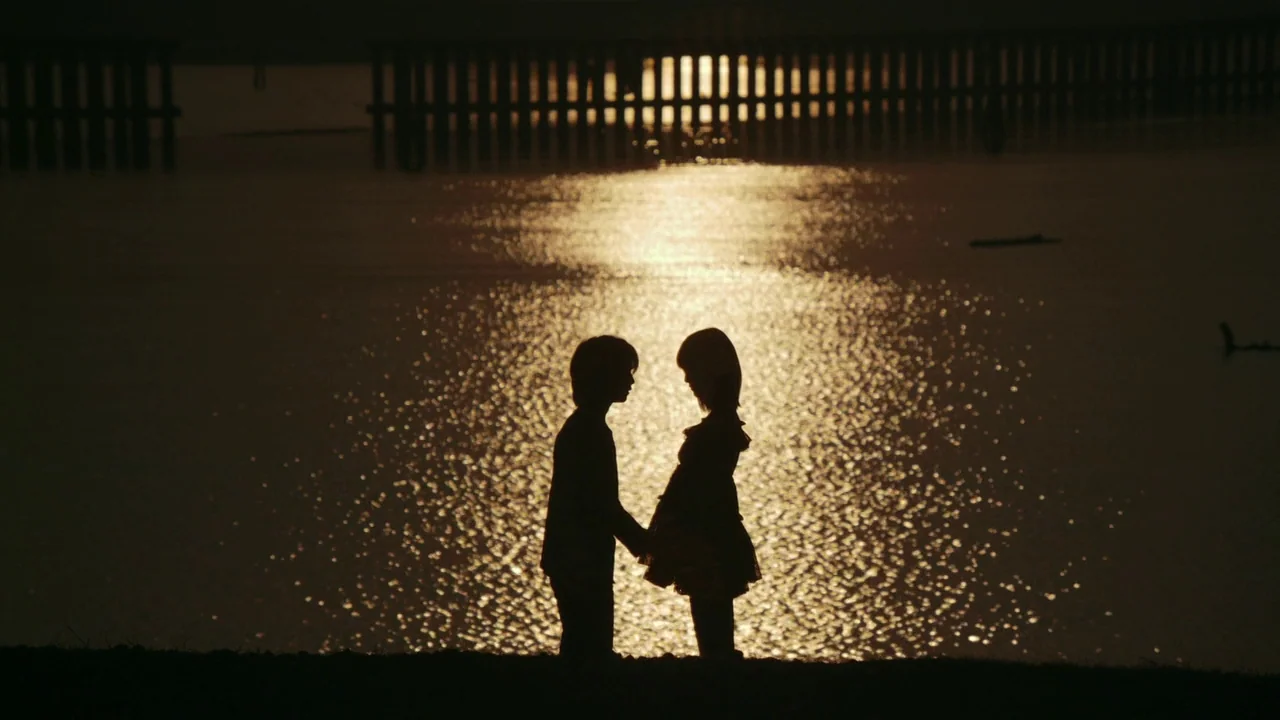 Confessions (2010) movie still: fullbody — A silhouette of two figures standing together on the dark edge of a lake. A wooden fence is visible in…