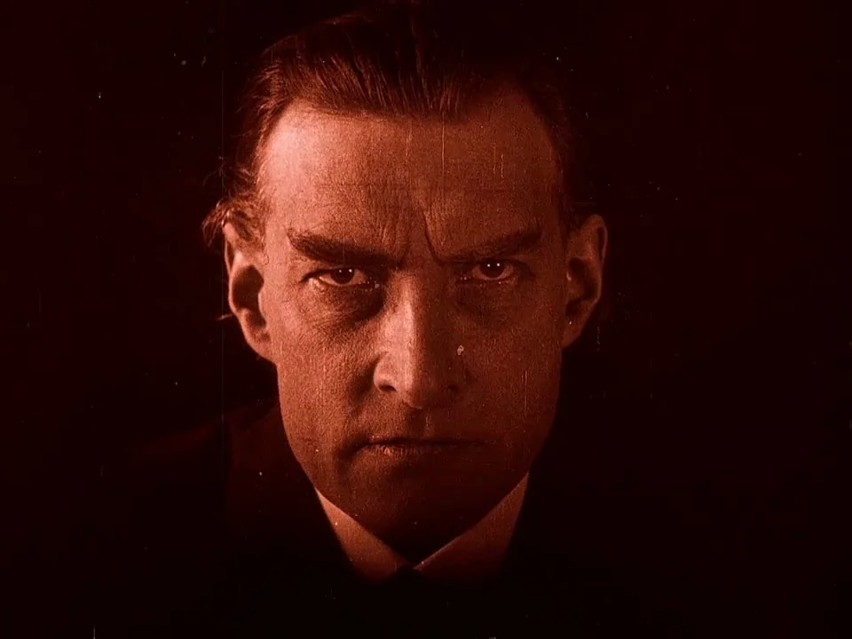 Häxan (1922) movie still: closeup — A close-up shot against a dark void reveals a man's face in high contrast. The man looks directly at the camera…