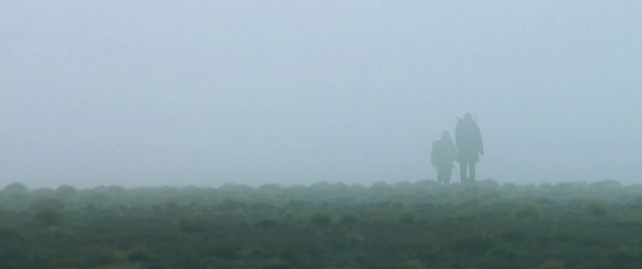 Hunt for the Wilderpeople (2016) movie still: wide — A vast, flat landscape covered in low grasses is engulfed in thick gray fog. Two figures walk…