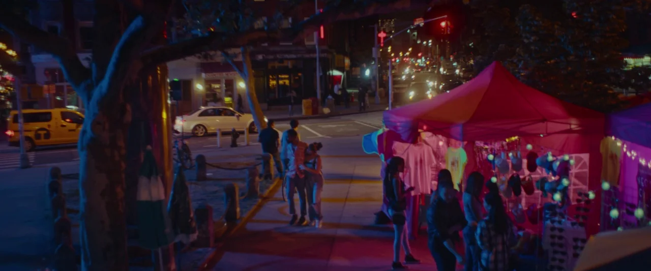 Someone Great (2019) movie still: wide — A nighttime city sidewalk features a red-canopied merchandise stall illuminated by artificial lights.…