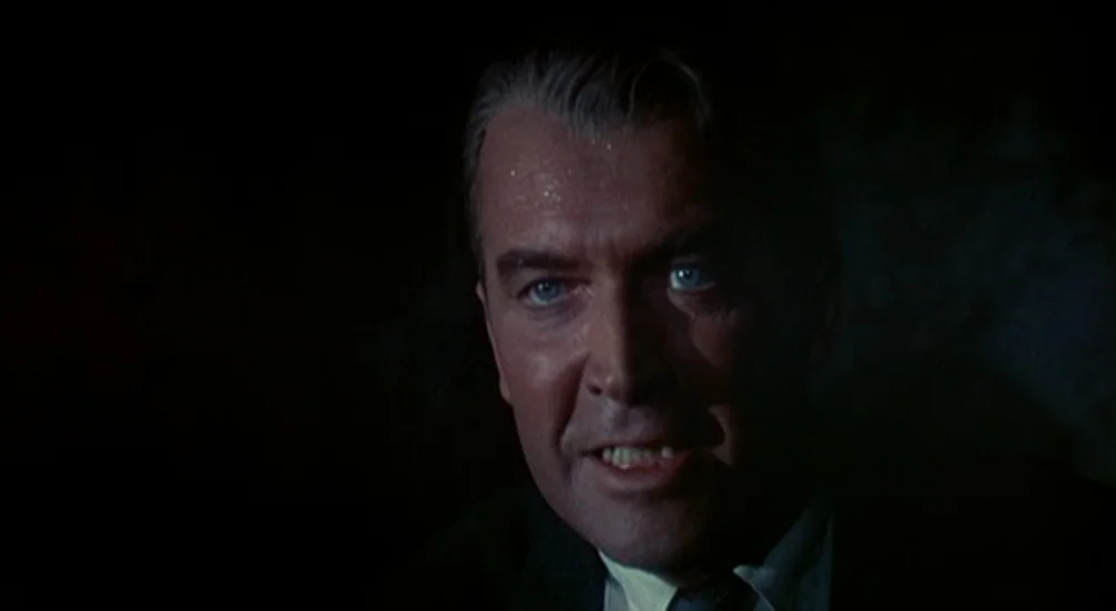 Vertigo (1958) movie still: closeup — A man's face is illuminated in a dark, shadow-filled environment. He speaks while looking directly forward…