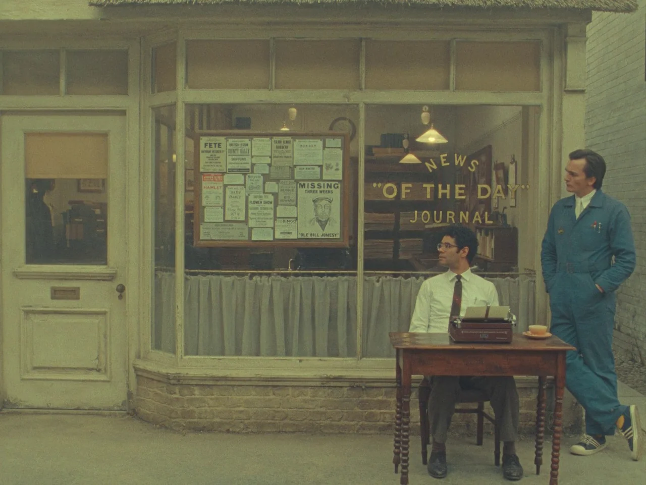 The Rat Catcher (2023) movie still: wide — A quaint mid-century storefront displays a notice board with various advertisements and missing posters.…