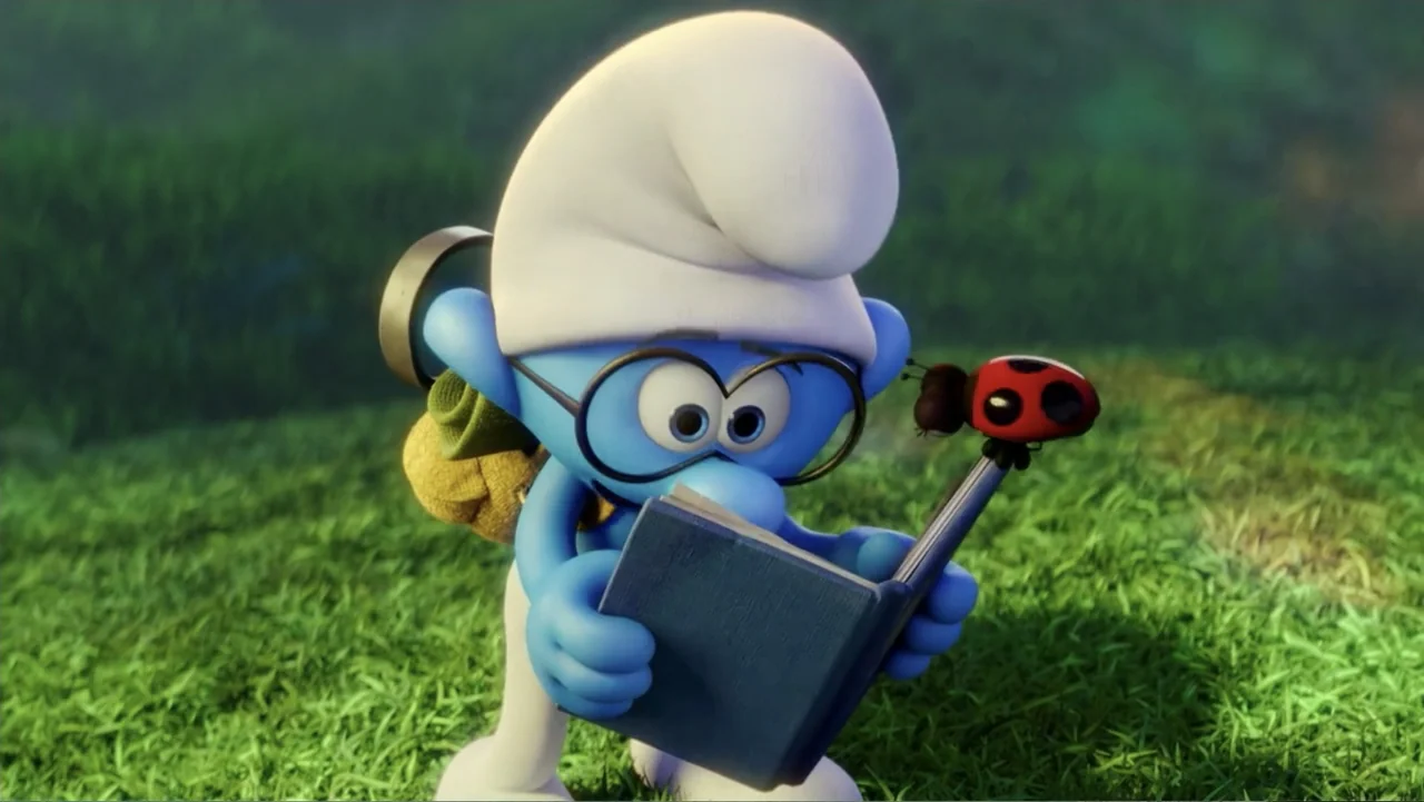 Smurfs: The Lost Village (2017) movie still: medium — A blue Smurf character stands in a lush green grassy field holding a book. The small character…