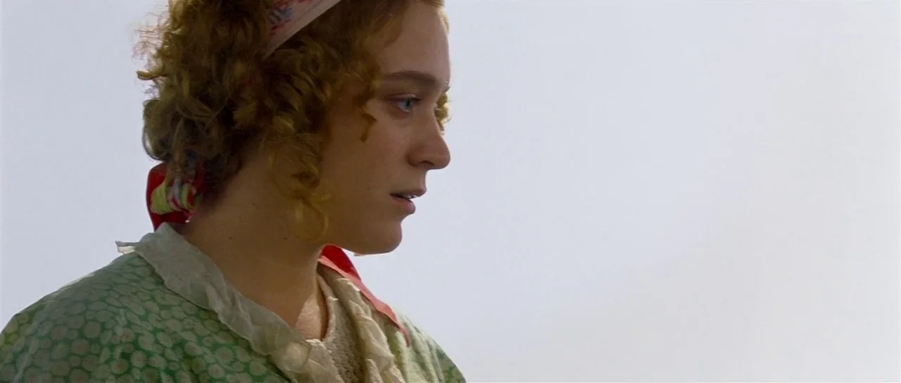 Dogville (2003) movie still: closeup — A woman stands in a bright, overcast outdoor field in historical attire. She looks off-screen toward the side…
