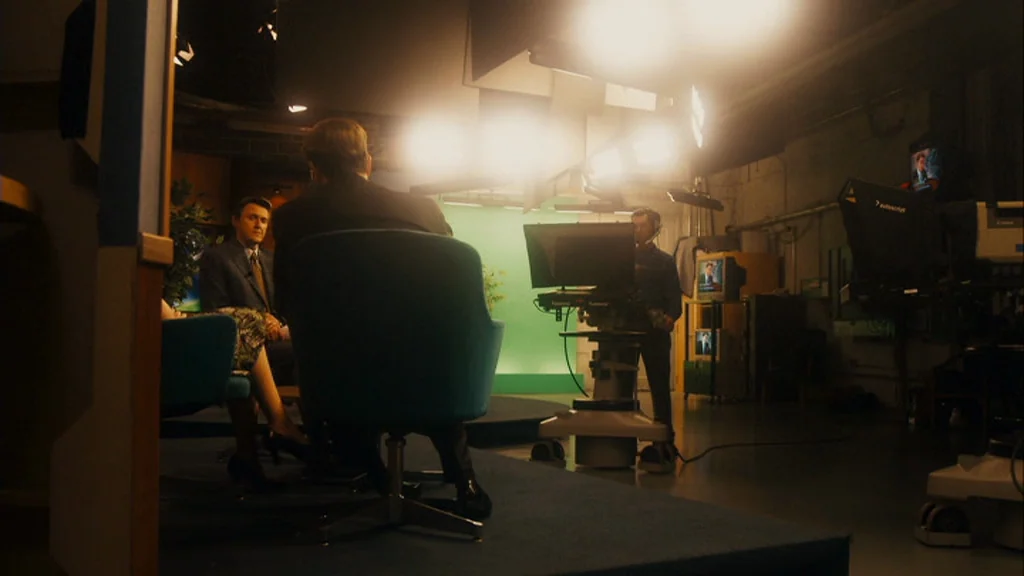 The Informant! (2009) movie still: wide — A television studio features blue carpeting and a green screen background. A host and guest sit in chairs…