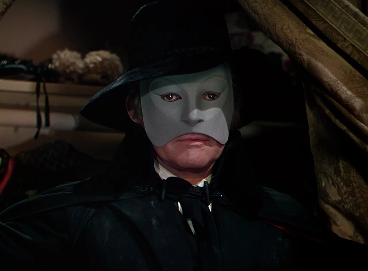 Phantom of the Opera (1943) movie still: closeup — An interior space contains a person wearing a theatrical mask and wide-brimmed hat. The subject…