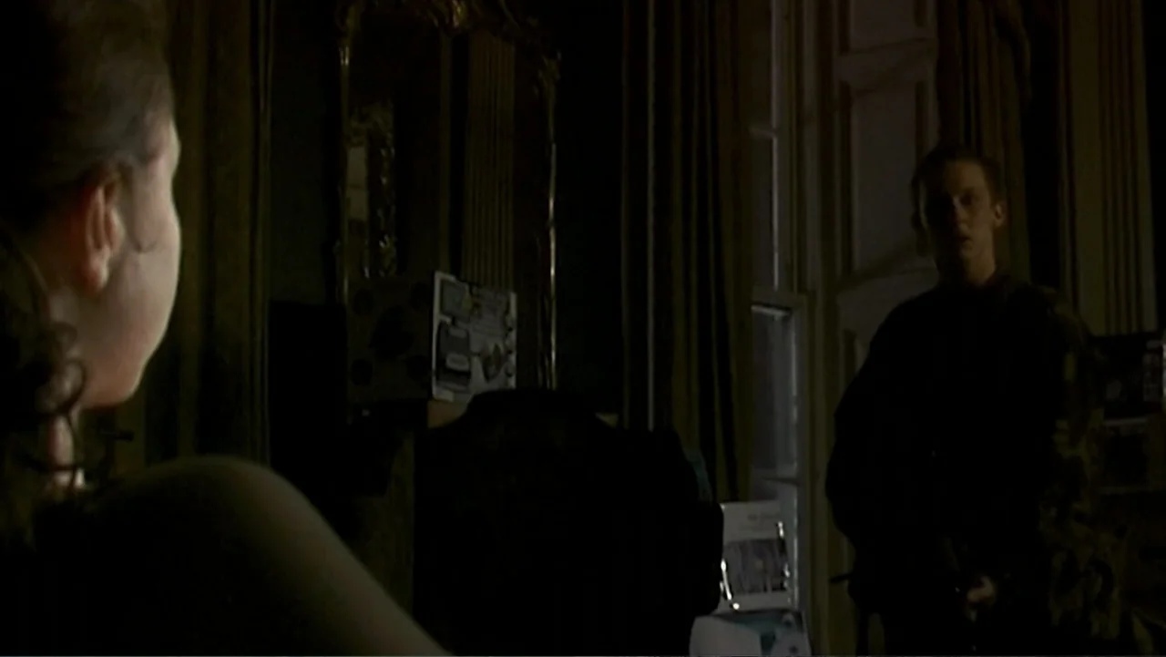 28 Weeks Later (2007) movie still: medium — A dark, sparsely furnished interior with heavy curtains covering a window. A man stands in the shadow of…