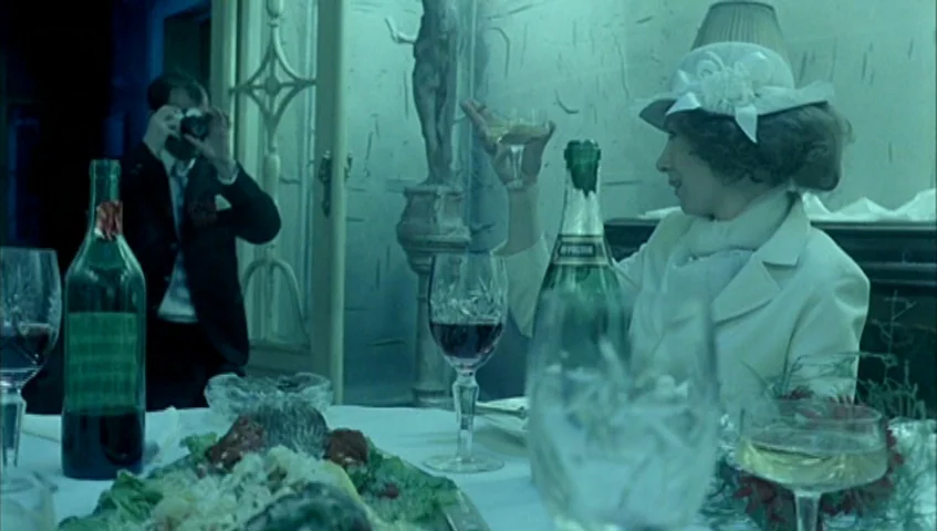 Almanac of Fall (1984) movie still: medium — A formal dining room table is set with wine glasses, a bottle, and food. A woman in a hat raises a…