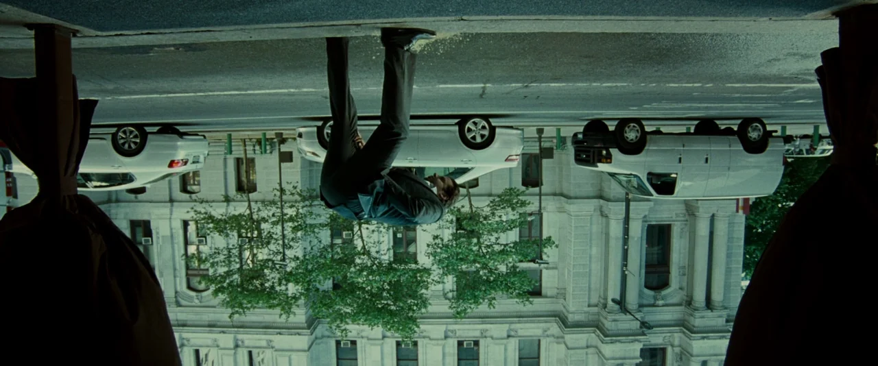 Limitless (2011) movie still: wide — An inverted urban city street scene with a government building in the background. A man in a business suit…