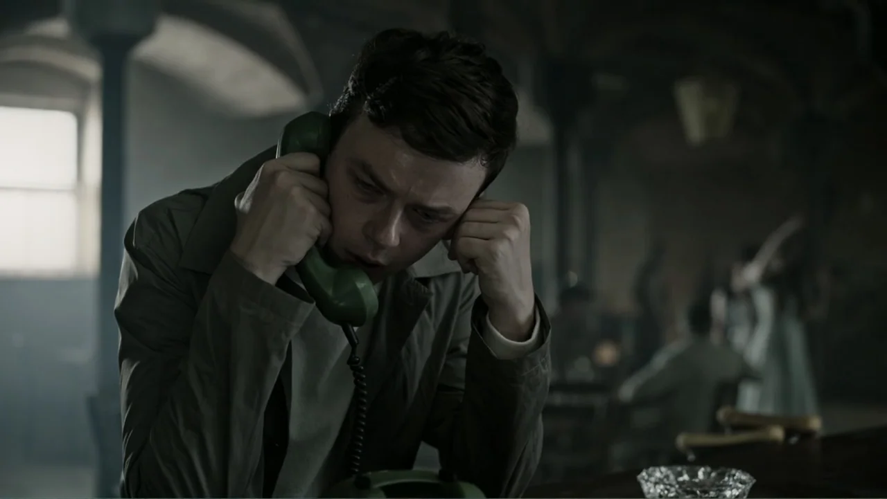 A Cure for Wellness (2017) movie still: medium — A dark, dimly lit bar with shadows obscuring the background and architectural features. A man in a…